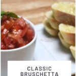 A bowl filled with classic tomato bruschetta recipe that's on a plate with ciabatta garlic bread.