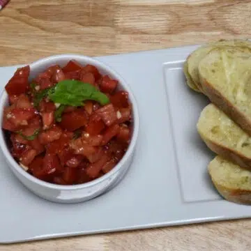 Overhead image of a bowl filled with classic bruschetta recipe and garlic toast.