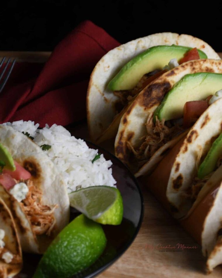 Overhead image of shredded crockpot chicken tacos on a plate with rice and limes.