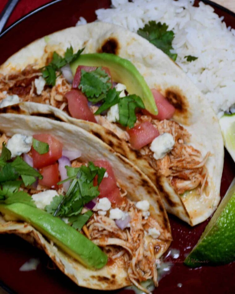 A close up of two slow cooker chicken tacos on a plate with rice and limes slices.