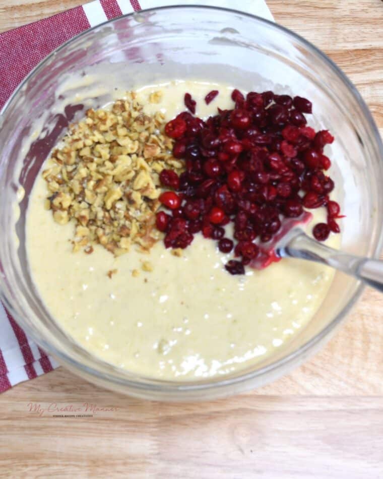 A bowl with the bread batter that has fresh chopped cranberries and walnuts on top of it.