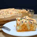 A slice of Halloween poke cake on a plate with cool whip and spinkles