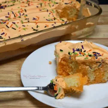 Orange poke cake that has orange cool whip and Halloween sprinkles on it that is on a plate.
