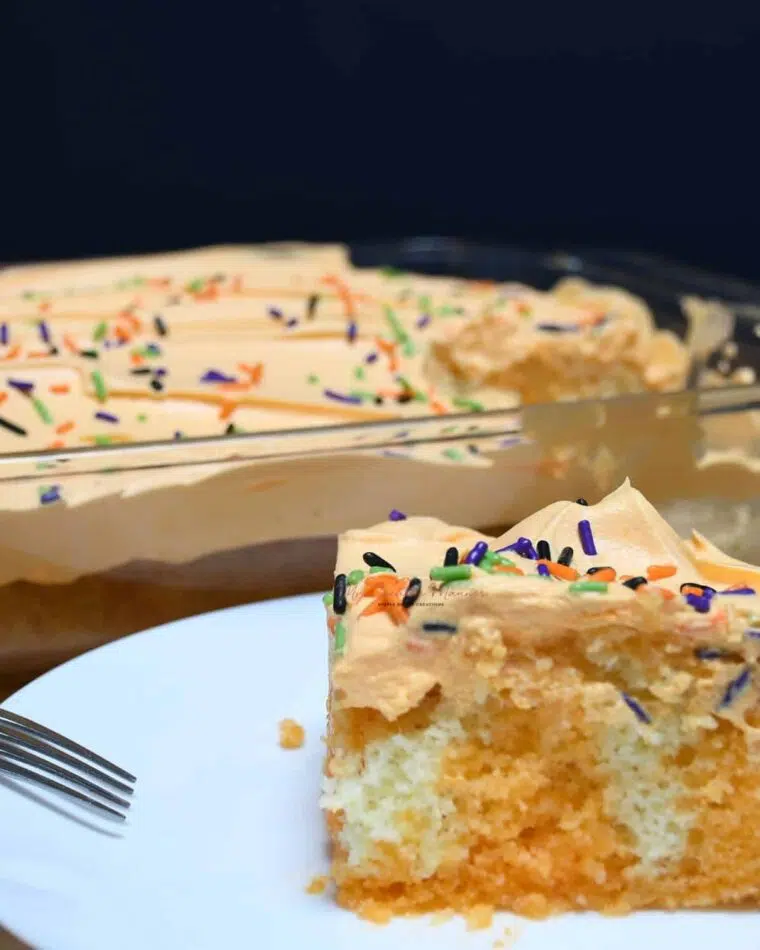 A slice of orange jello poke cake with orange cool whip with Halloween sprinkles on it.