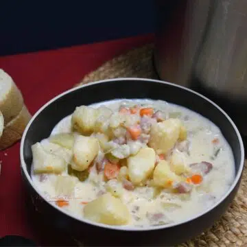 A bowl filled with crockpot ham and potato soup that has carrots and celery in it.