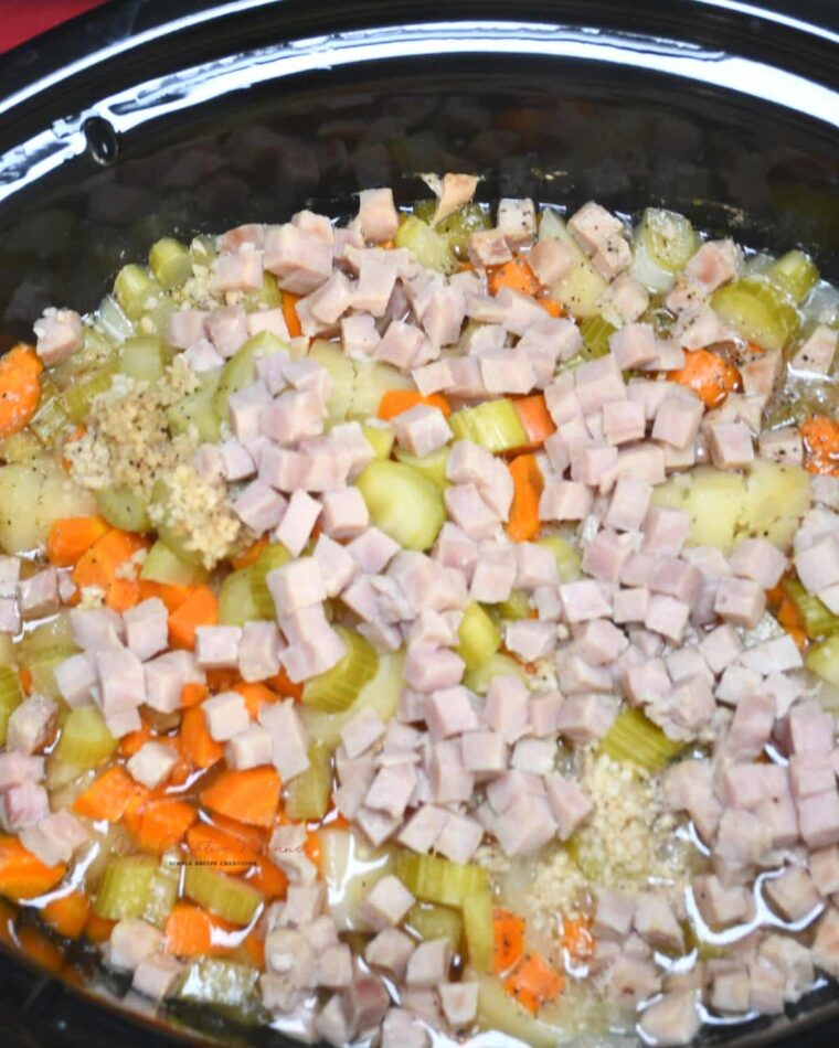 A crock pot fill with diced ham, potatoes, carrots, celery, onions, and garlic for potato and ham soup.