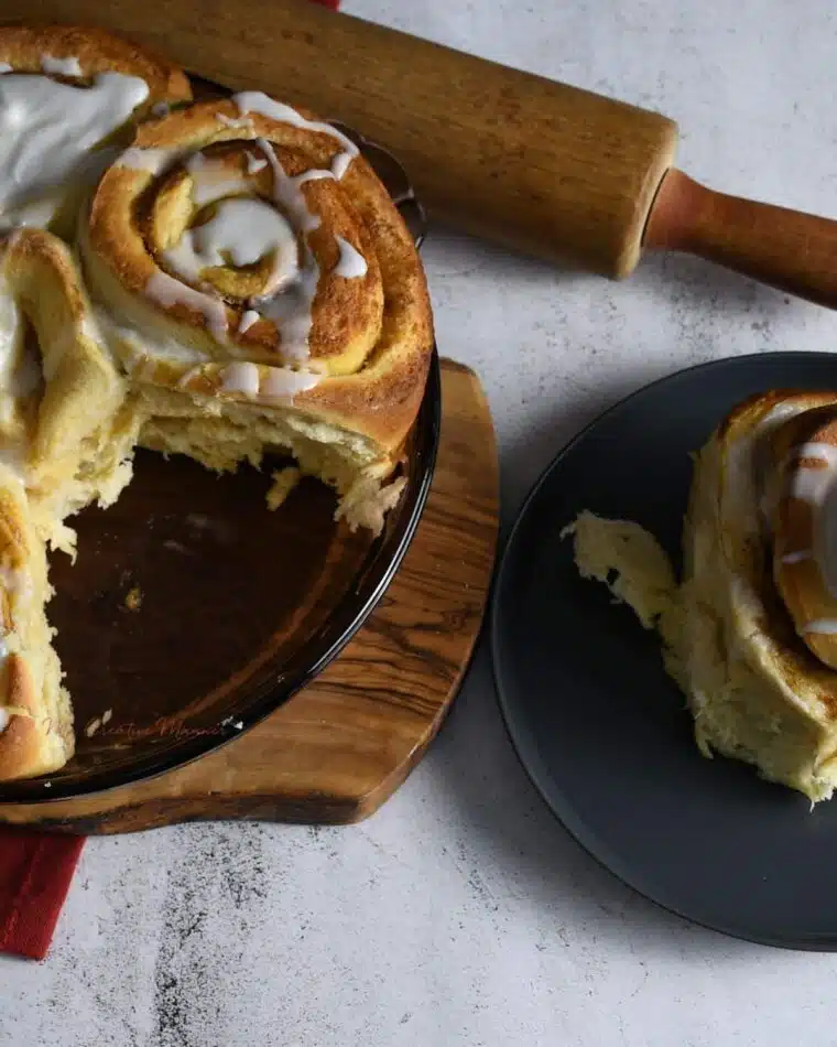 Overhead image of a baking dish filled with pumpkin butter cinnamon rolls with one on a plate.