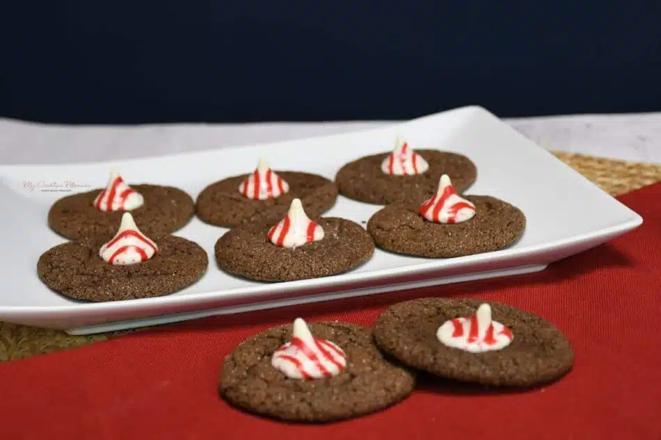 Two chocolate peppermint kiss cookies on a napkin with more in a plate.