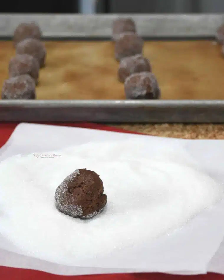 A close up of a chocolate thumbprint cookie dough ball that is being rolled in sugar.