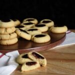 Raspberry jam thumbprint cookies on a wood board.