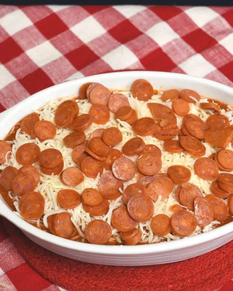 Mini pepperonis on top of pizza dip that hasn't been baked yet.