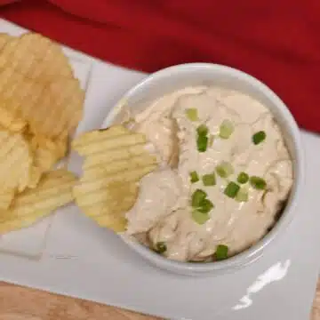A bowl with a chip and the 3 ingredint onion dip recipe in it with more chips on the plate next to the bowl.