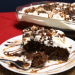 A slice of moist chocolate turtle cake on a plate that has carmale and chocolate sauce on it.