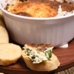 A slice of garlic toast with spinach artichoke crab dip on it.