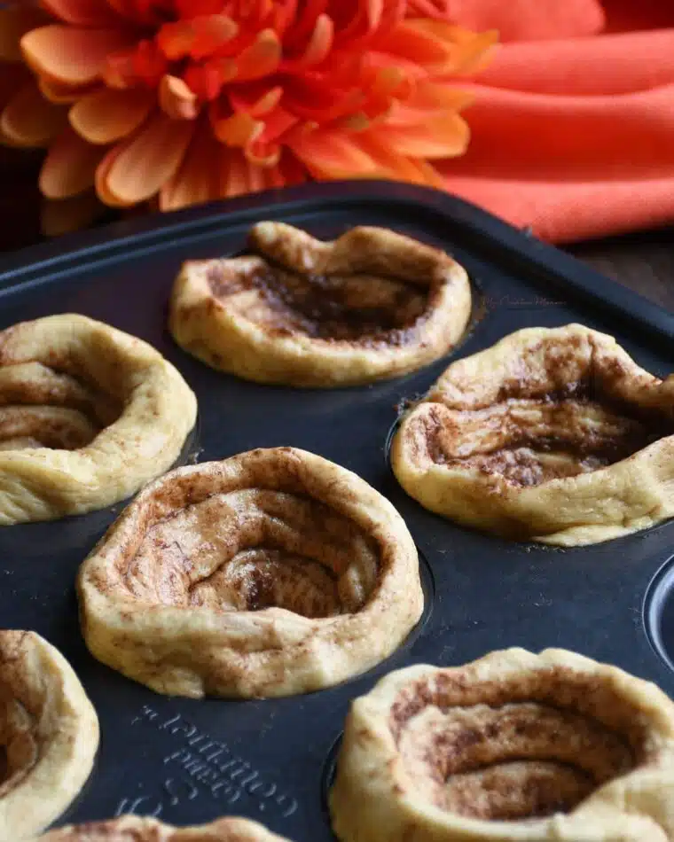 Cinnamon buns pressed into a muffin tin before its been filled with canned apple pie filling.