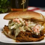 A close up of 2 ingredient pulled pork on a bun that is topped with cheese and coleslaw.