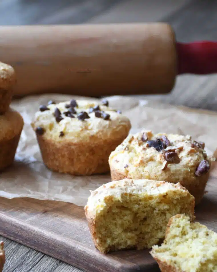 A close up of a 2 ingredeint banana muffin that has been spilt in half. With more in the background that has been topped with chocolate chips or nuts.