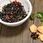 Fresh blueberry salsa on a pita chip with more in a large white bowl.