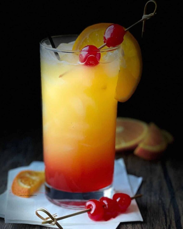 A close up of the cocktail recipe in a glass that has been garnished with an orange slice and maraschino cherries.