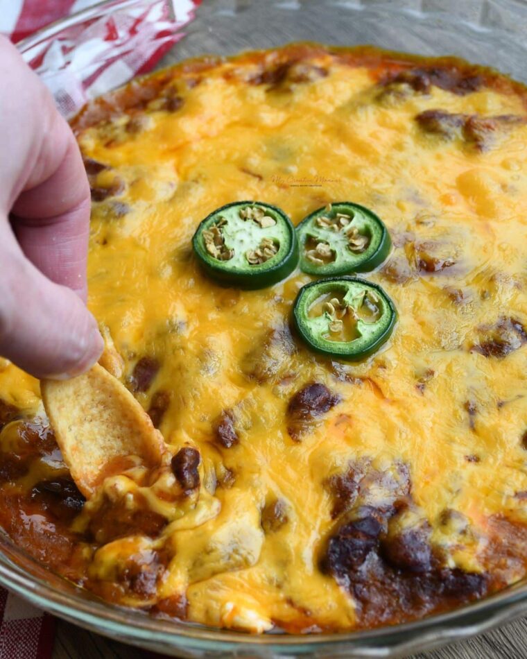 A hand scooping the chili cheese dip recipe with a Fritos scoops corn chip.