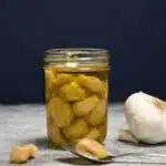 A jar with garlic confit in it and a garlic clove on a spoon.