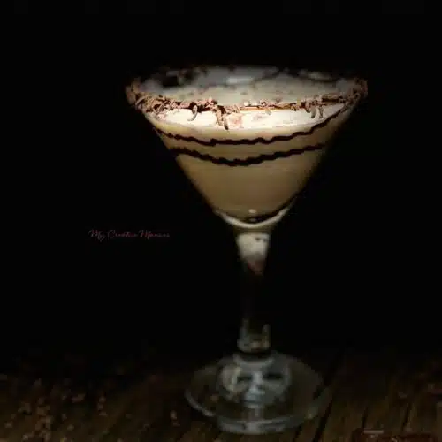 A single glass that is filled with chocolate martini with chocolate syrup and shavings around the rim of the glass.