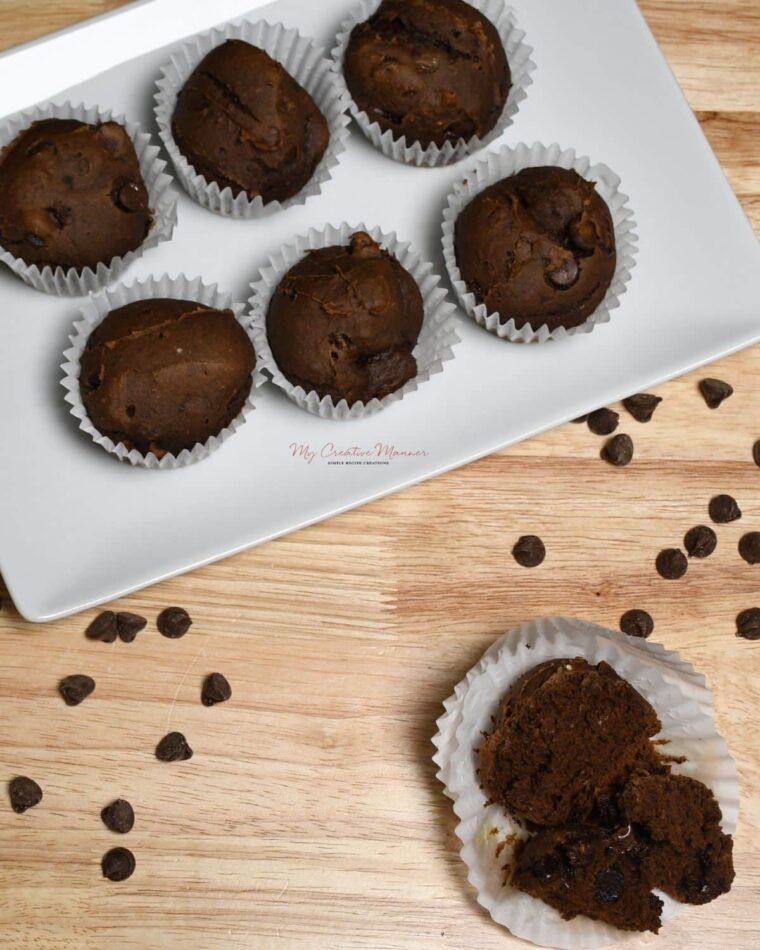 Overhead image of a plate that has the pumpkin muffins on it with another chocolate pumpkin muffin that is split in half in front of the plate.