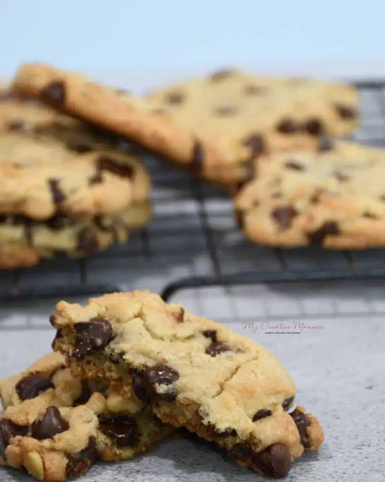 A close up of a walnut chocolate chip cookie that has been split in half, with more cookies on a cooling rack.