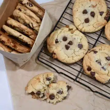 Overhead image of salted caramel chocolate chip cookies on a wire rack and some in a paper bag.
