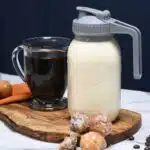 A jar filled with homemade coffee cream with a glass of coffee next to it and donuts in front of the jar.