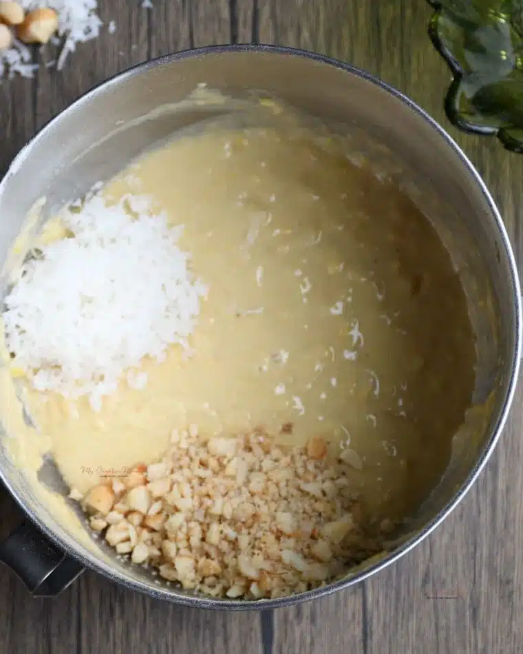 Top view of a large bowl that is filled with the batter for the pineapple banana bread with coconut and macadamia nuts on top.