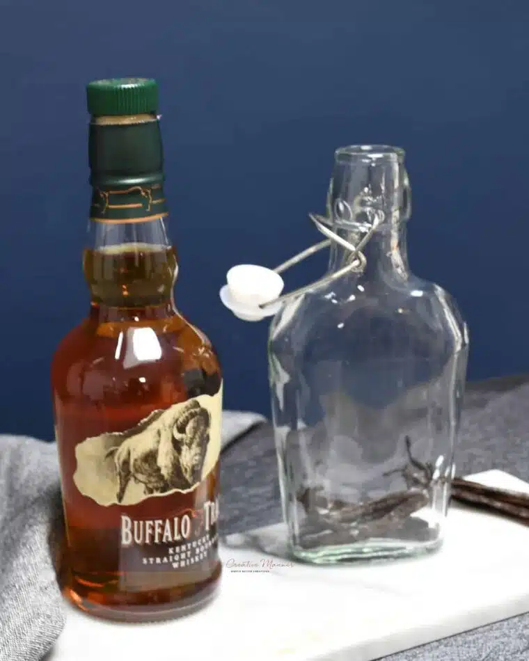 A bottle that has vanilla beans in it and a bottle of bourbon next to it.