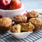 Apple cinnamon muffins on a cooling rack with one cut in half.