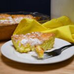 A close up of a slice of two ingredient lemon bar on a plate with more bars in a baking dish.