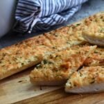 A close up of an Italian bread that has been turned into crispy parmesan garlic bread that is on a wood plate.