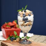 A tall glass filled with layers of yogurt, fruit, and granola to make a healthy Greek yogurt parfait.