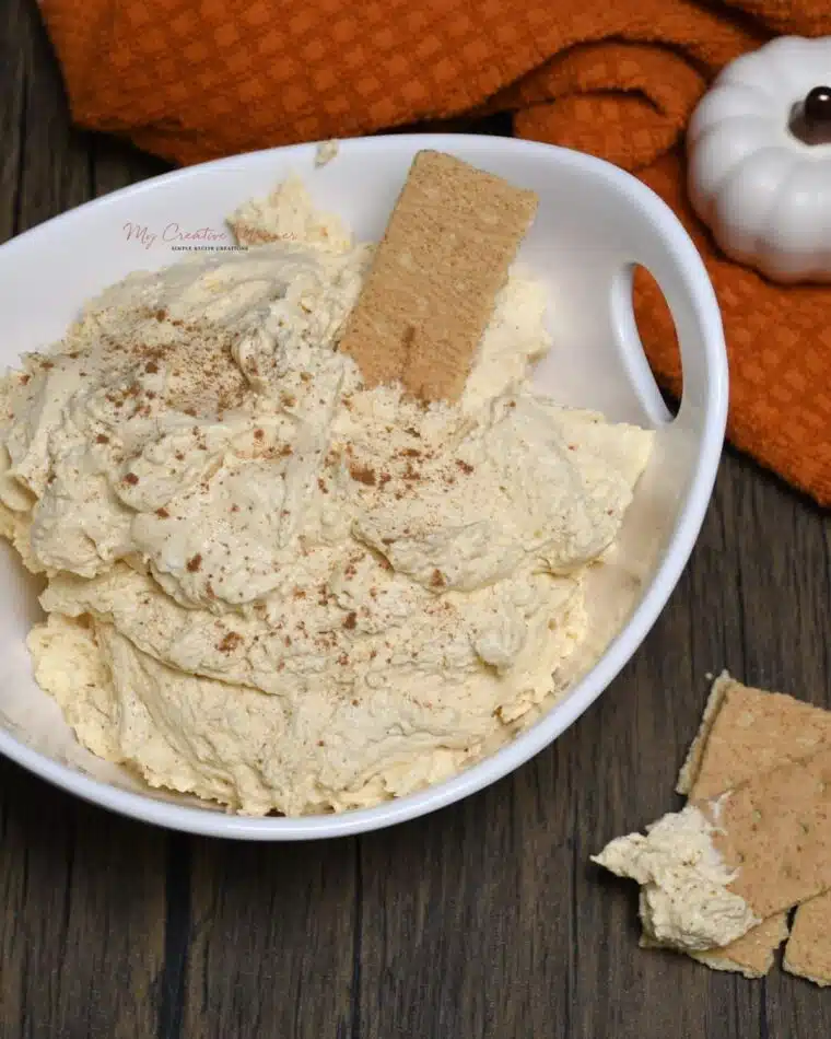 Overhead image of the pumpkin dip in a white bowl with a cracker in it.