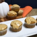 Close up of pumpkin spice latte muffins on a white plate with more stacked behind the plate.