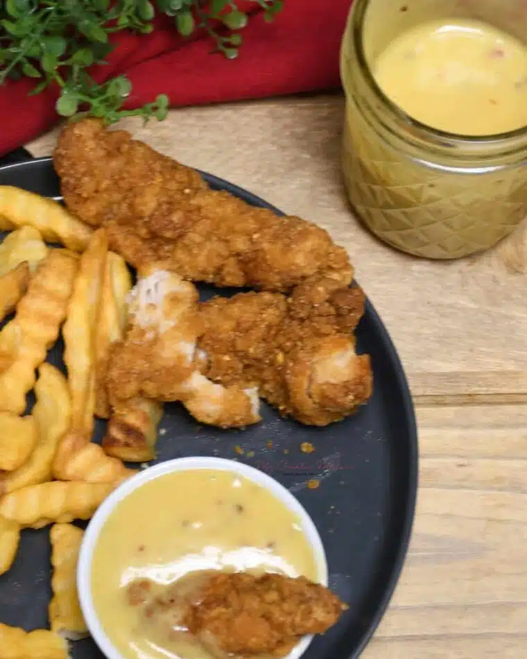 Overhead of a small dish that has a chicken tender dipped into the sauce. With more of the honey mustard sauce in a jar.