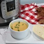 Closeup of a of acorn squash soup with an Instant Pot behind it and bread next to the bowl.