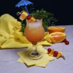 Front view of the Malibu drink recipe in a tall glass with a umbrella straw with cherries and orange chunks on a skewer.