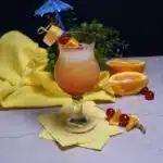 Front view of the Malibu drink recipe in a tall glass with a umbrella straw with cherries and orange chunks on a skewer.