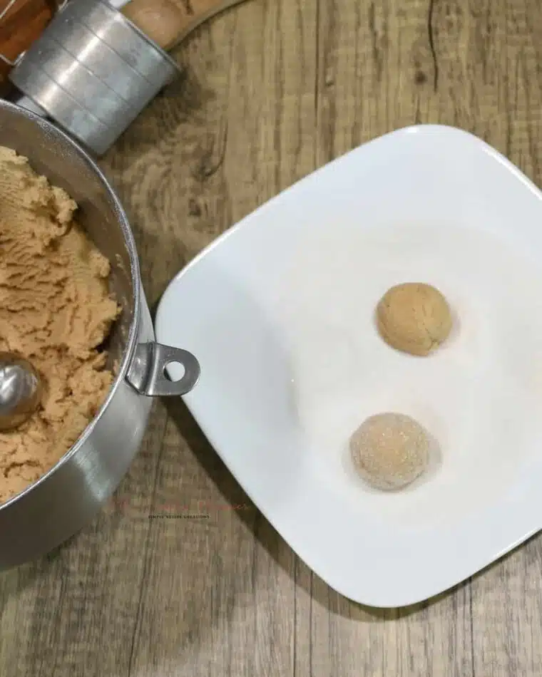 Two gingerbread dough balls being rolled in sugar.