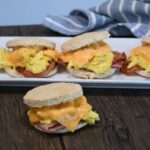 Bacon, egg, and cheese breakfast sandwiches on a plate and one in front of the plate.
