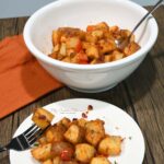 A bowl filled with the roasted potatoes and more on a plate that is in front of the bowl.