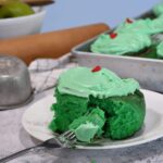 A close up of a green cinnamon roll with green frosting and a red heart sprinkle on it.