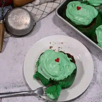 Overhead image of a green cinnamon bun on a plate with a fork that has some of the roll on it.