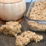 Close up of two pumpkin spice rice krispie treats on a counter with more in a baking dish next to them.