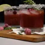 Close up of a cocktail glass that has a salted rim and garnished with fresh cranberries and a sprig of rosemary.