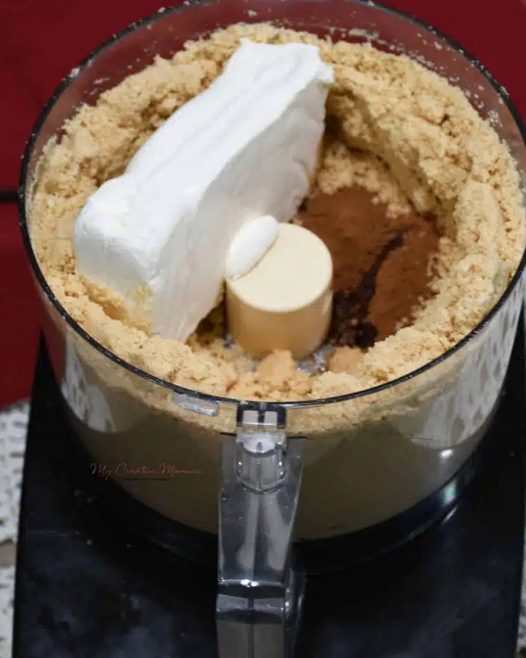 Golden Oreo crumbles with a block of cream cheese in a food processor.